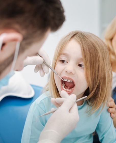 a pediatric dentist checking a child patient’s teeth