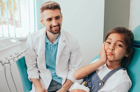 a child holding her cheek while visiting her dentist