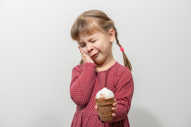 child eating an ice cream cone and wincing