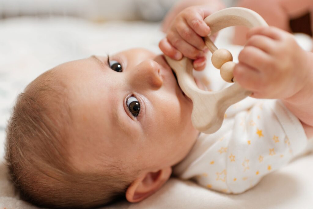 Baby in onesie with stars chewing on wooden teething ring